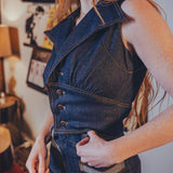 Person wearing a funky 70s inspired denim vest and high waisted bellbottom jeans in an indoor setting with decor.