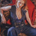 Woman sitting on a patterned rug with a red blanket and guitar in the background