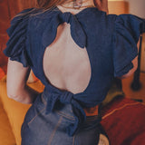 Person wearing a blue top with open back and puffed sleeves.