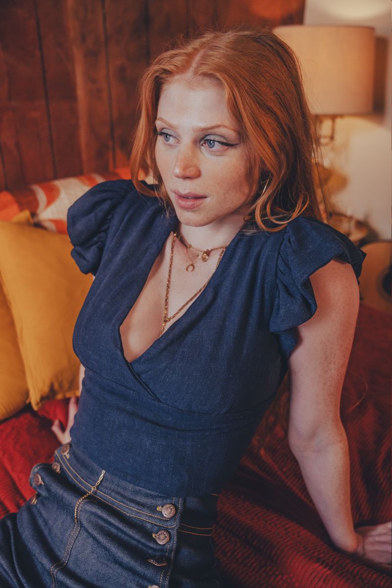 Woman in a blue top sitting on a couch with a warm-toned lamp in the background