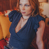 Woman in a blue top sitting on a couch with a warm-toned lamp in the background