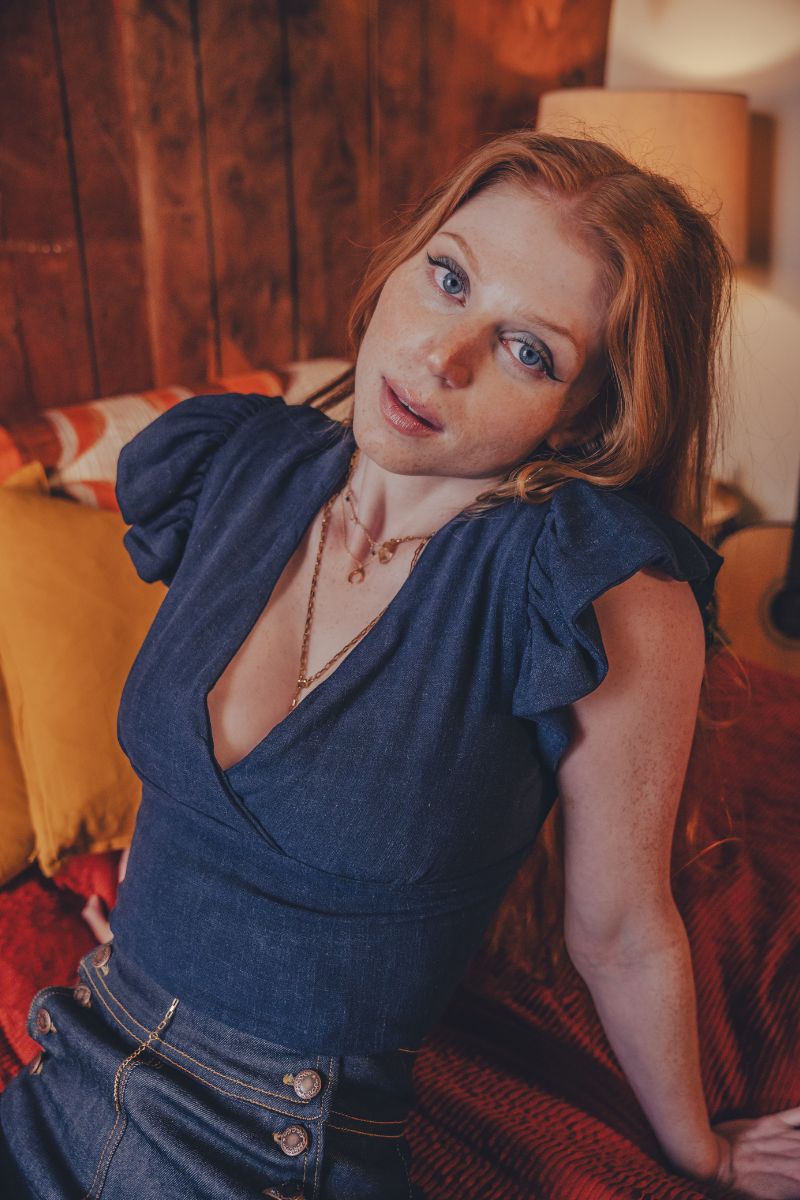 Woman in a blue top sitting on a couch in a warm-toned room.