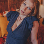 Woman in a blue top sitting on a couch in a warm-toned room.