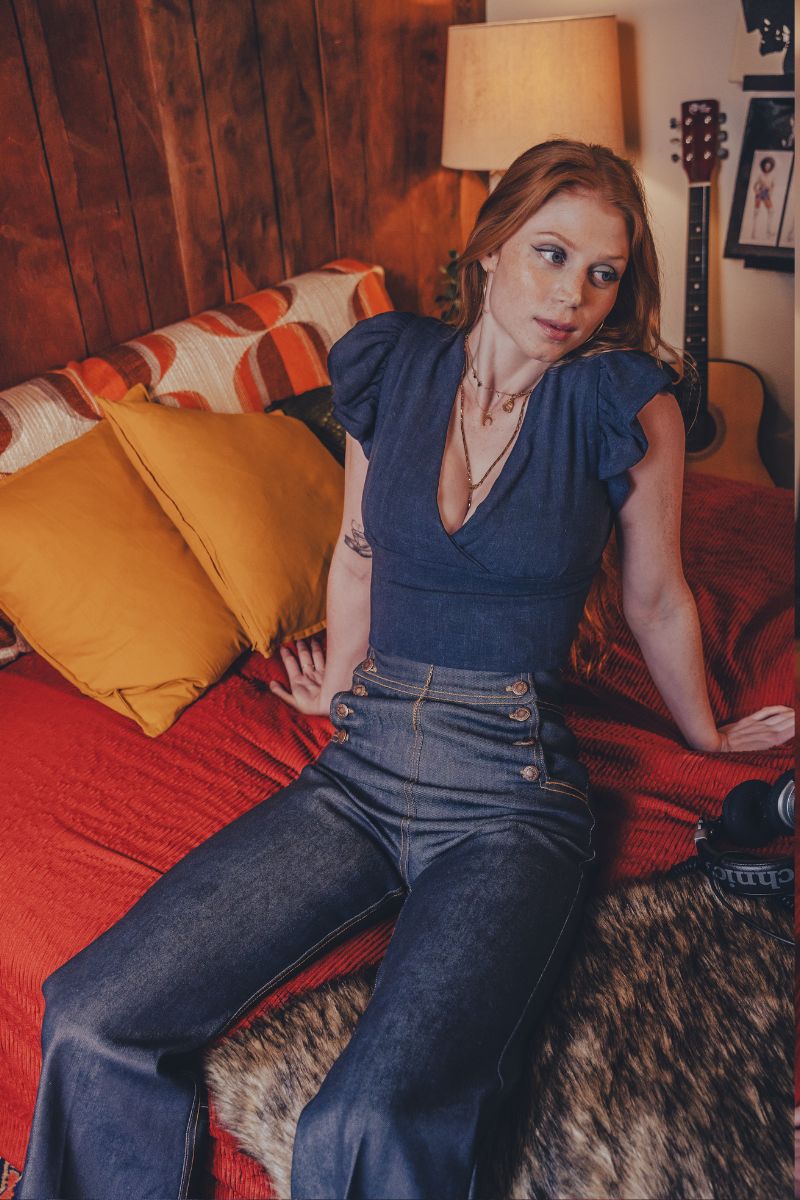 Woman sitting on a bed in a room with wooden walls and a guitar in the background