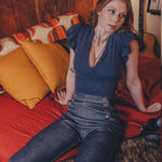 Woman sitting on a bed in a room with wooden walls and a guitar in the background