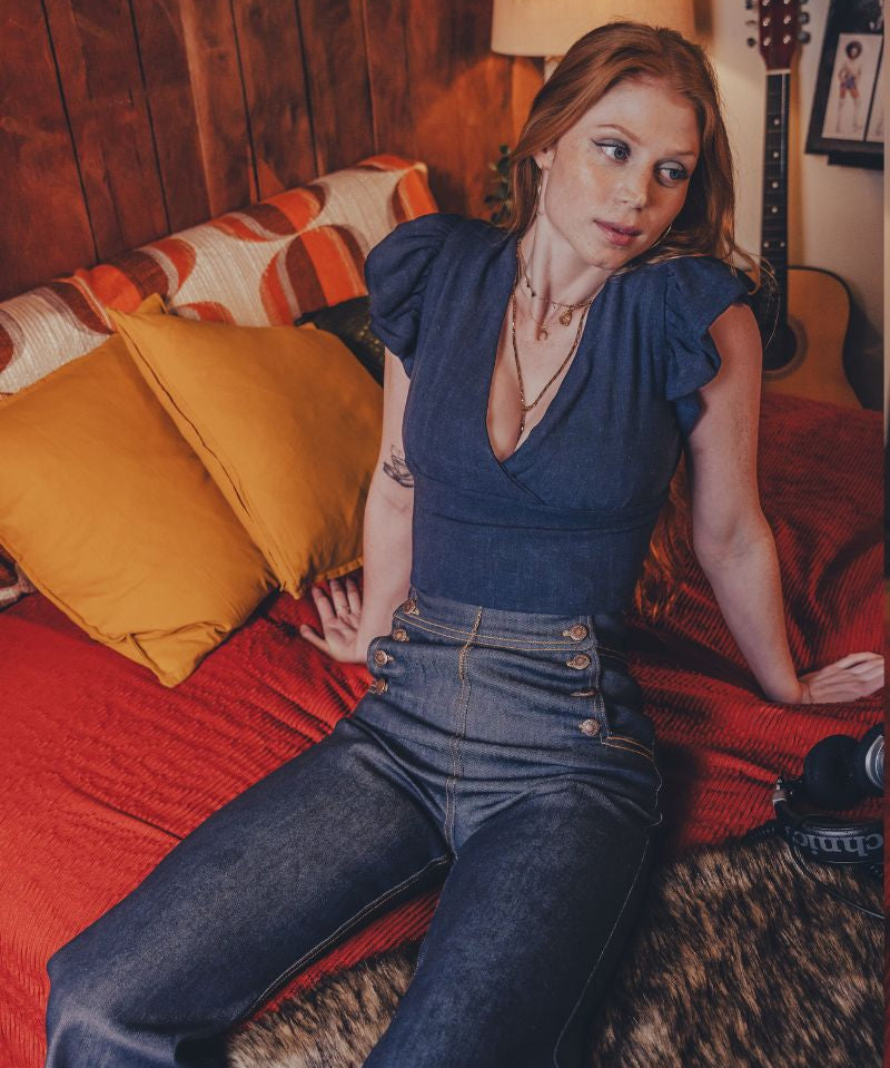 Woman sitting on a bed in a room with wooden walls and a guitar in the background