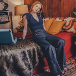 Woman sitting on a couch in a cozy living room with a guitar and lamp in the background.