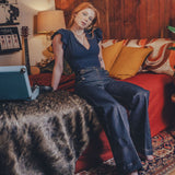 Woman sitting on a couch in a cozy living room with a guitar and lamp in the background.