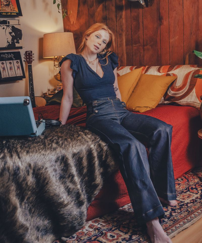 Woman sitting on a couch in a cozy living room with a guitar and lamp in the background.