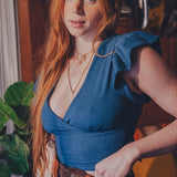 Woman with long red hair wearing a blue top and brown pants in an indoor setting.