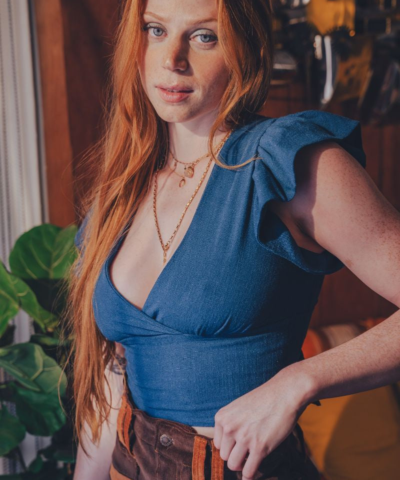 Woman with long red hair wearing a blue top and brown pants in an indoor setting.