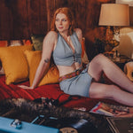 Woman in a 1970s inspired denim outfit sitting on a couch in a cozy room with a lamp and pillows.