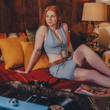 Woman in a 1970s inspired denim outfit sitting on a couch in a cozy room with a lamp and pillows.