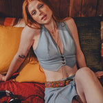 Woman sitting on a retro 1970s style couch wearing a light denim top and denim mini skirt with a woodstock inspired flower power colorful belt.