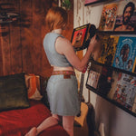 Person in a room with 70s vinyl records and a guitar wearing Soul Sister since 1969 small batch clothing made in Vancouver Canada