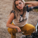 Woman in a sleeveless top and yellow pants sitting on a motorcycle outdoors wearing Soul Sister since 1969.
