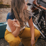 Woman in yellow pants sitting next to a motorcycle with a cigarette in her hand wearing Soul Sister since 1969.