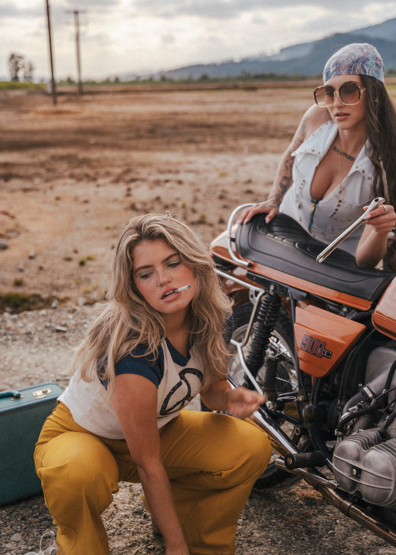 Two women with a motorcycle in an open field with mountains in the background wearing Soul Sister since 1969