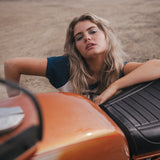 Woman leaning on an orange motorcycle in a desert-like setting 