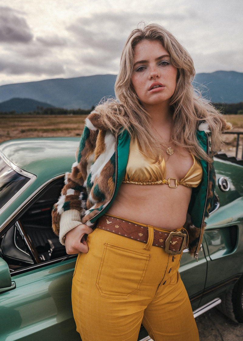 Woman in a vintage outfit standing next to a classic car with mountains in the background wearing soul sister since 1969
