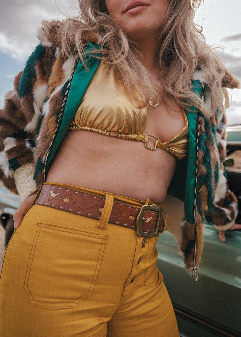 Person wearing a gold top and mustard pants with a patterned jacket wearing soul sister since 1969.