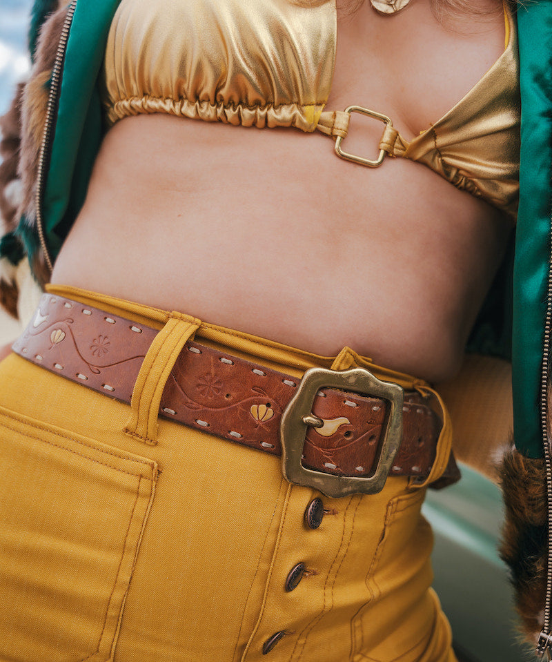 Person wearing a gold top and yellow pants with a brown belt wearing soul sister since 1969.