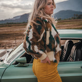Woman in a patterned coat and yellow pants standing next to a vintage car with mountains in the background wearing Soul Sister since 1969