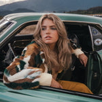 Woman sitting in a vintage car with mountains in the background wearing Soul Sister since 1969