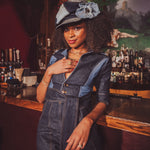 Woman in a denim outfit with a hat standing behind a bar.