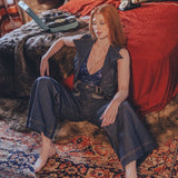 Woman sitting on a patterned rug in a bedroom with a red bedspread and colorful pillows.