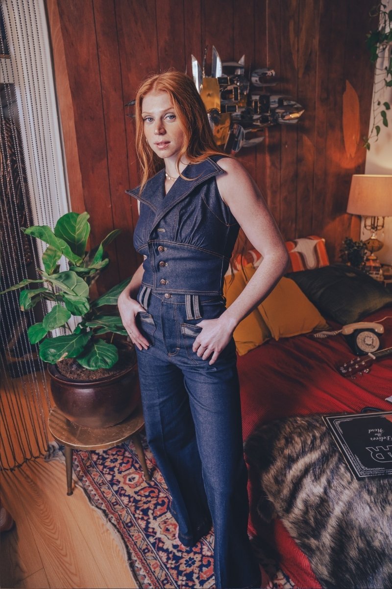 Woman in a denim outfit standing in a room with wooden paneling and decorative elements.