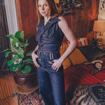 Woman in a denim outfit standing in a room with wooden paneling and decorative elements.
