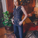 Woman in a denim outfit standing in a room with wooden paneling and decorative elements.