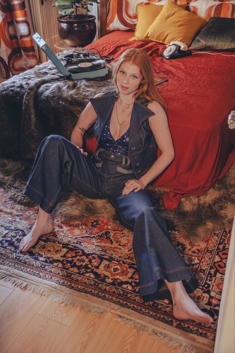 Woman sitting on a patterned rug in a room with a red bedspread and vintage decor.