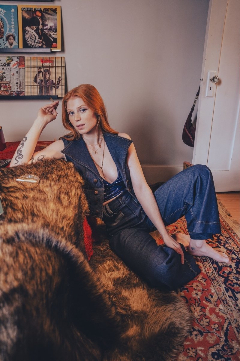 Woman sitting on a fur-covered couch in a room with posters on the wall.