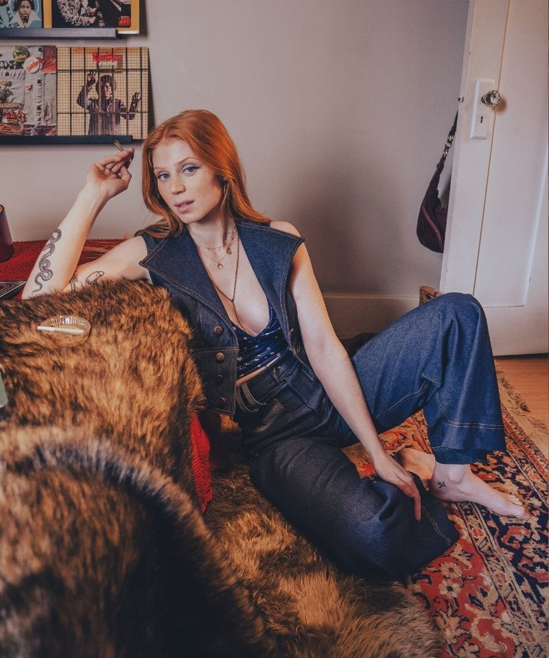 Woman sitting on a fur-covered couch in a room with posters on the wall.