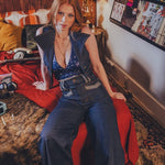 Woman sitting on a bed in a room with posters and a lamp.