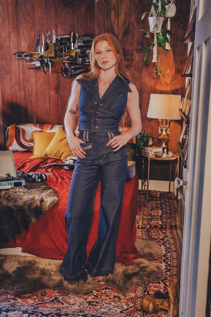 Woman in a blue outfit standing in a room with wooden walls and decorative items.