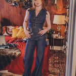 Woman in a blue outfit standing in a room with wooden walls and decorative items.