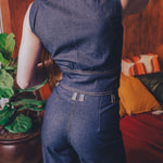 Person wearing a blue denim jumpsuit in a room with a plant and colorful cushions.