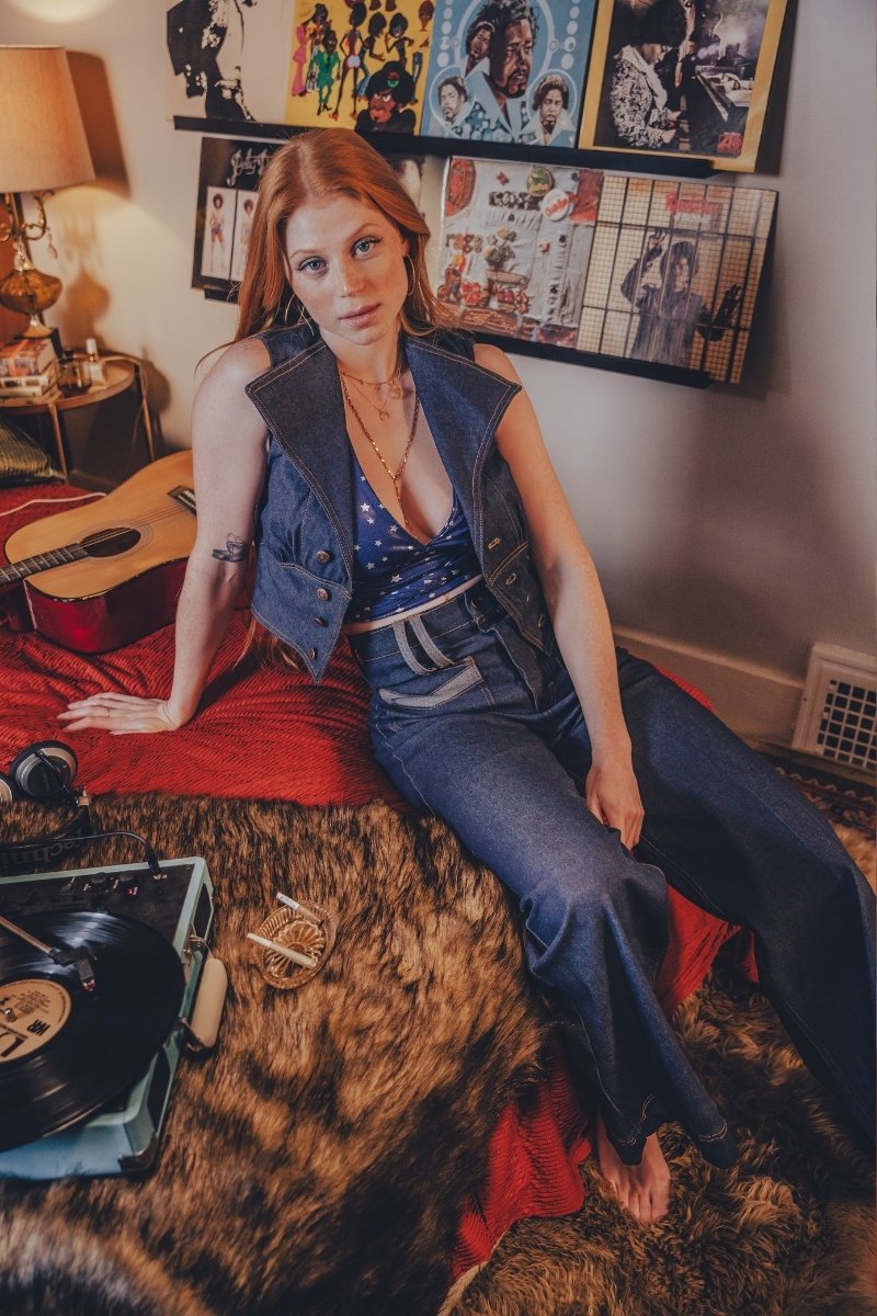 Woman sitting on a bed with a guitar and records, surrounded by wall art