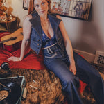 Woman sitting on a bed with a guitar and records, surrounded by wall art