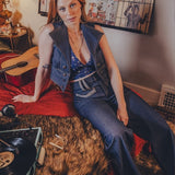 Woman sitting on a bed with a guitar and records, surrounded by wall art