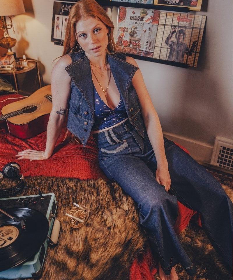 Woman sitting on a bed with a guitar and records, surrounded by wall art
