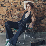  Side view of a 70s inspired backless denim jumpsuit with halter neckline and retro bell bottom legs