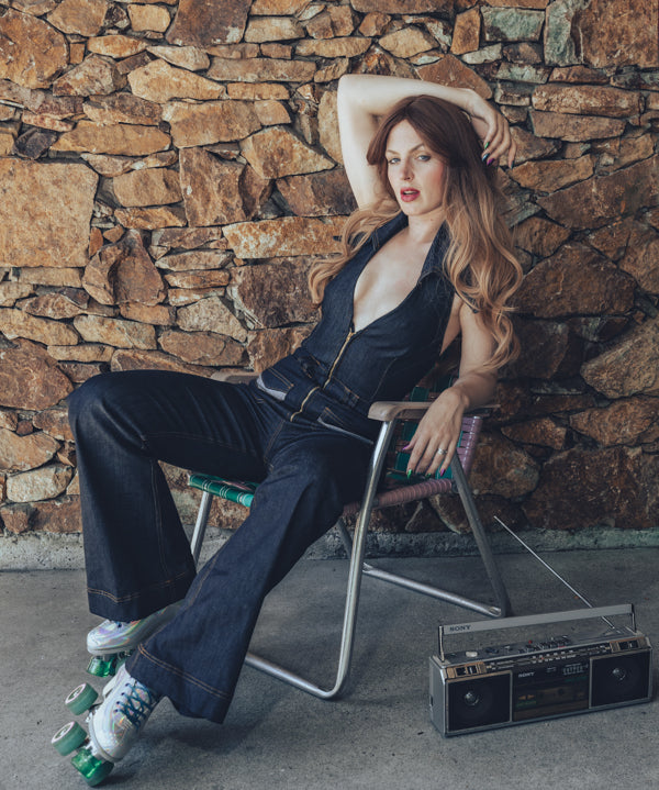  Side view of a 70s inspired backless denim jumpsuit with halter neckline and retro bell bottom legs