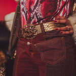 Close-up of a person wearing a patterned top and red pants with a gold belt and clutch.