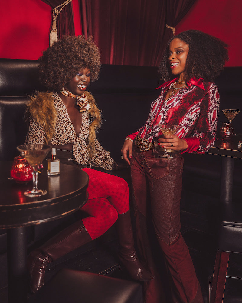 Two women sitting in a stylish bar setting with drinks and decor.