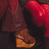 Brown wedge shoe with wooden sole worn by a person in red pants.
