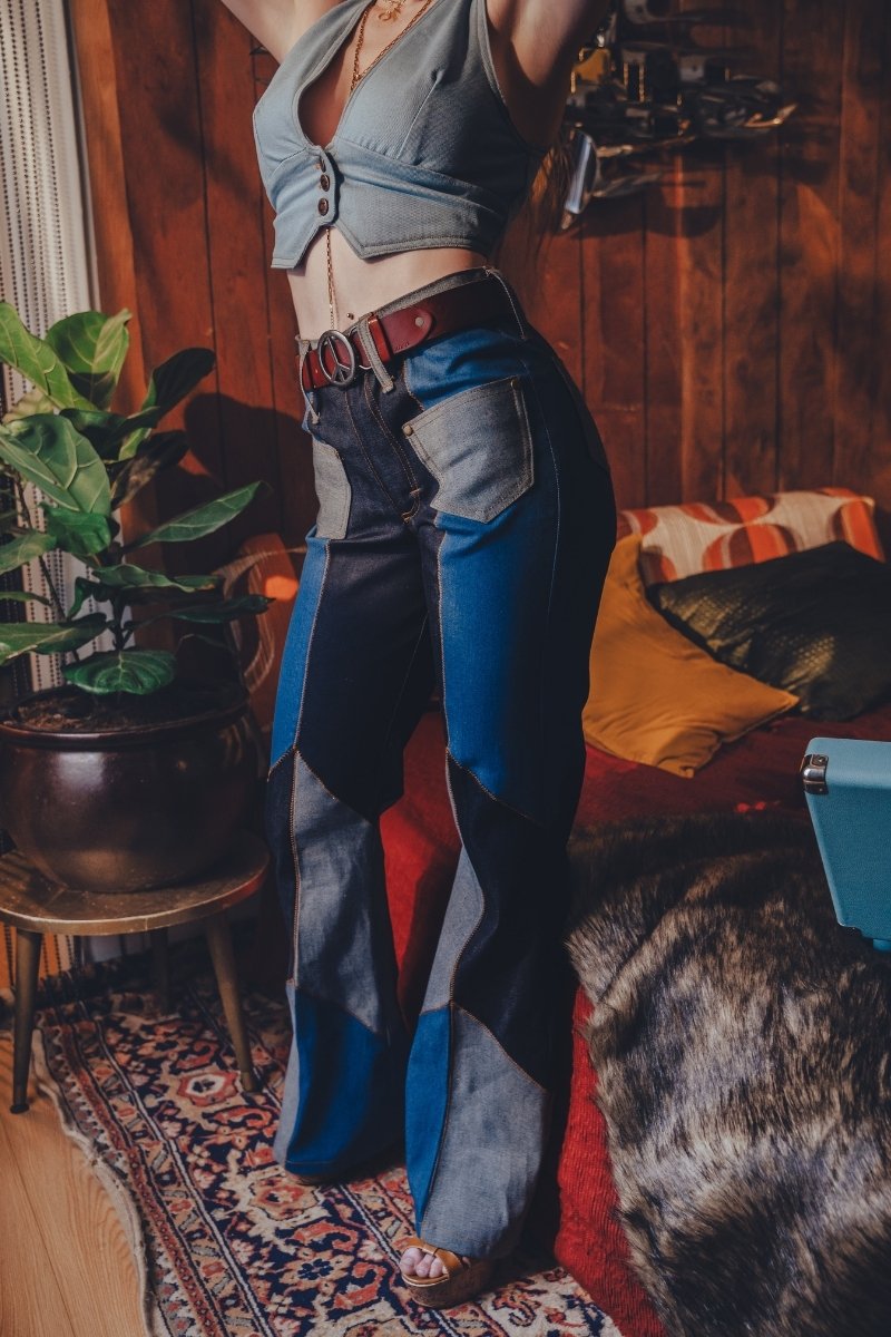 Person wearing a crop top and patchwork jeans in a room with wooden walls and a rug.